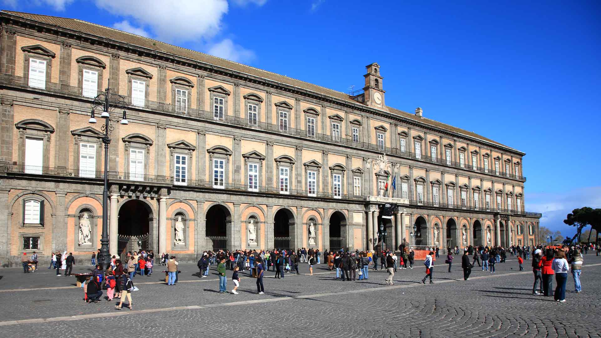 Exterior view of the Royal Palace of Naples, showcasing its grand façade and architectural details against a clear sky